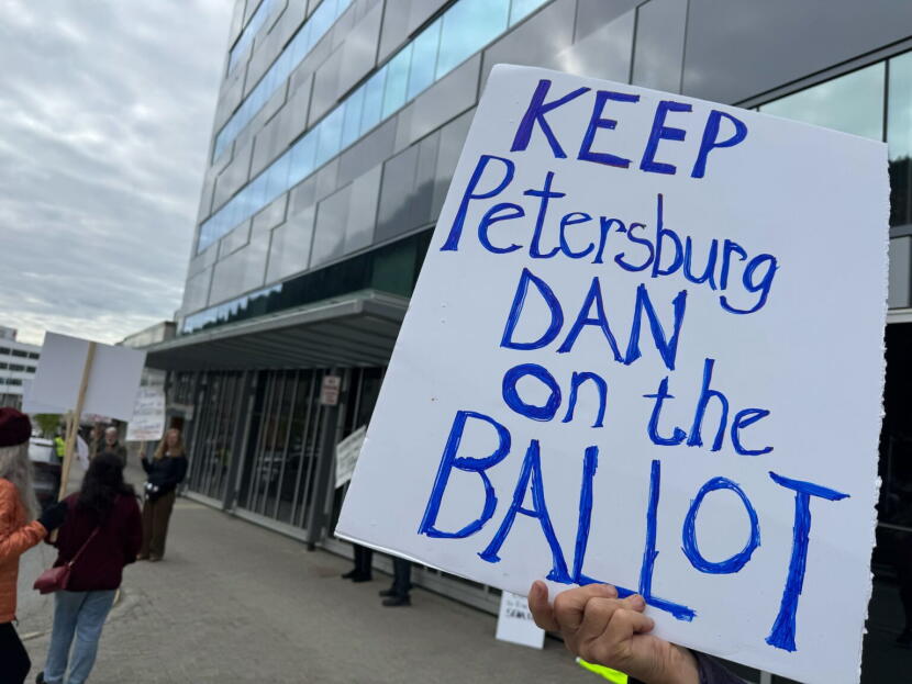A demonstrator holds a protest sign in support of Dan J. Sullivan of Petersburg after the Alaska Division of Elections issued a preliminary decision to remove the candidate from the ballot on June 12, 2026.
