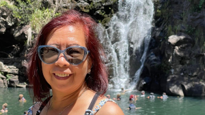 This is a photo of Lewelyn Dixon. She's wearing sunglasses and a sleeveless outfit, and she's standing in front of a waterfall.