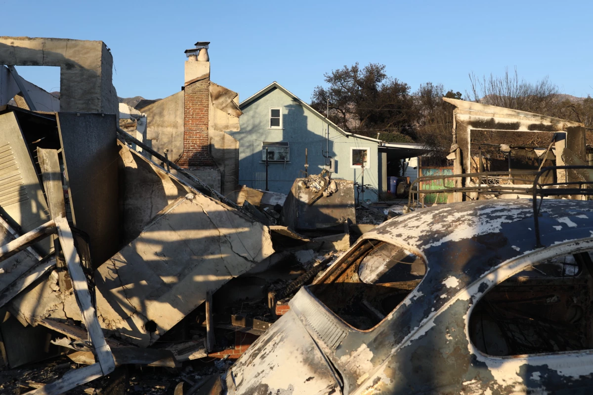 A teal house stands relatively unscathed behind a home destroyed by the Eaton Fire. An early analysis of the Los Angeles fires found that brush and wood fencing helped spread the fire from house to house.