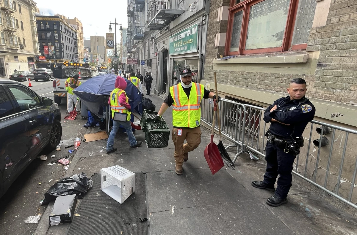 San Francisco police officers keep an eye on city workers as they sweep unsanctioned tents and belongings from a street in the Tenderloin.