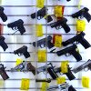 More than a dozen handguns are shown hanging on a display wall. Most are black and most have a yellow tag attached to them.