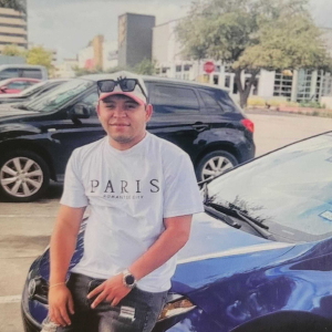 A man sits on the hood of a blue car while look at the camera.