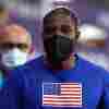 Olympic sprinter Noah Lyles wears a black KN95 mask and a blue t-shirt with an American flag on it.