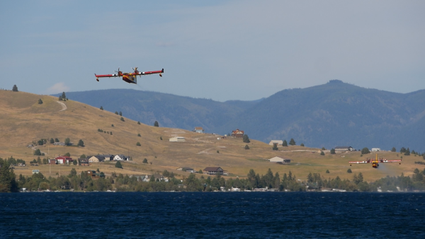 Two "Super Scooper" planes fly low above Montana's Flathead Lake on August 4, 2022. Mountains are visible in the background.