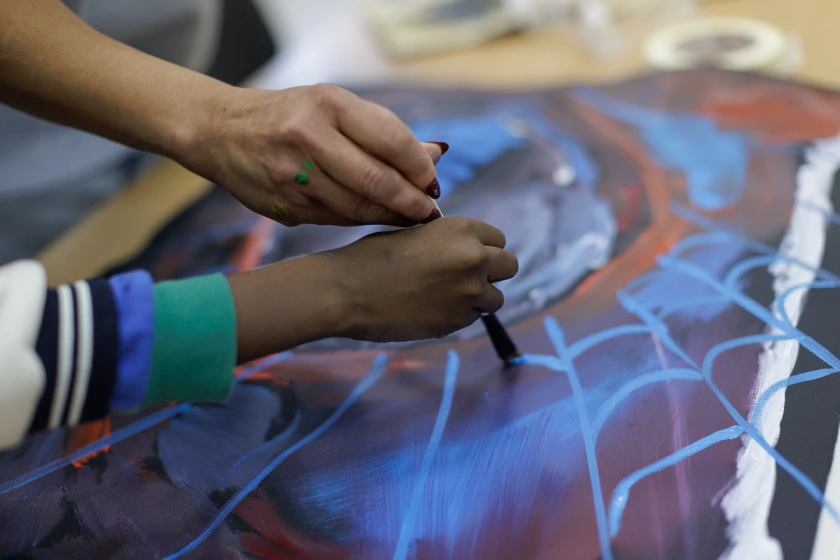 An art teacher paints with the 8-year-old son of Leila, a Nigerian mother, who didn't want to be photographed. She says he loves Spiderman, as his art here shows.