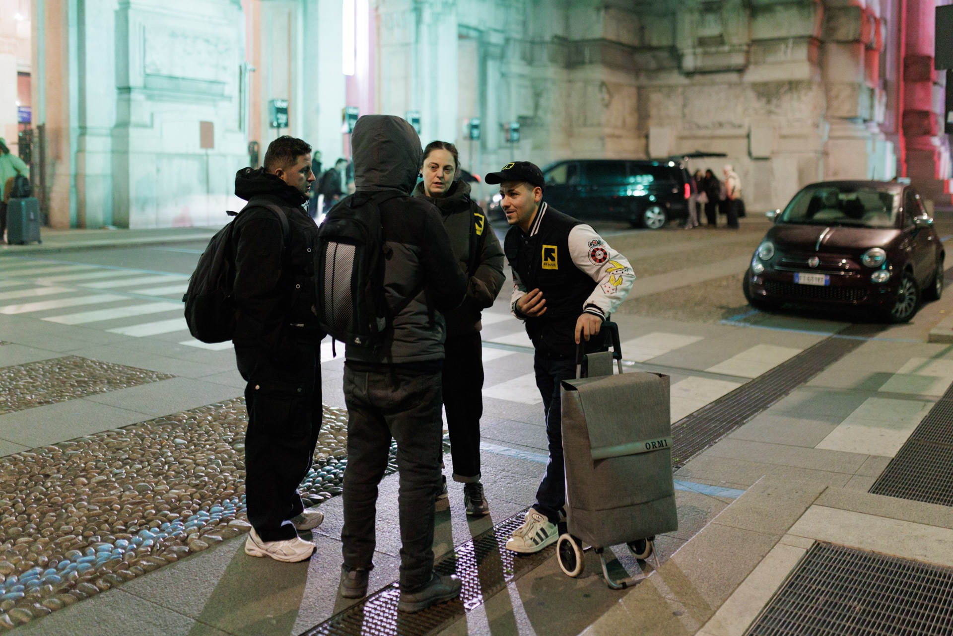 Outreach team members of an International Rescue Committee (IRC), an international humanitarian group, stand outside Milano Centrale railway station at night. The station remains a critical hub for migrants and homeless individuals seeking temporary refuge from the winter cold.