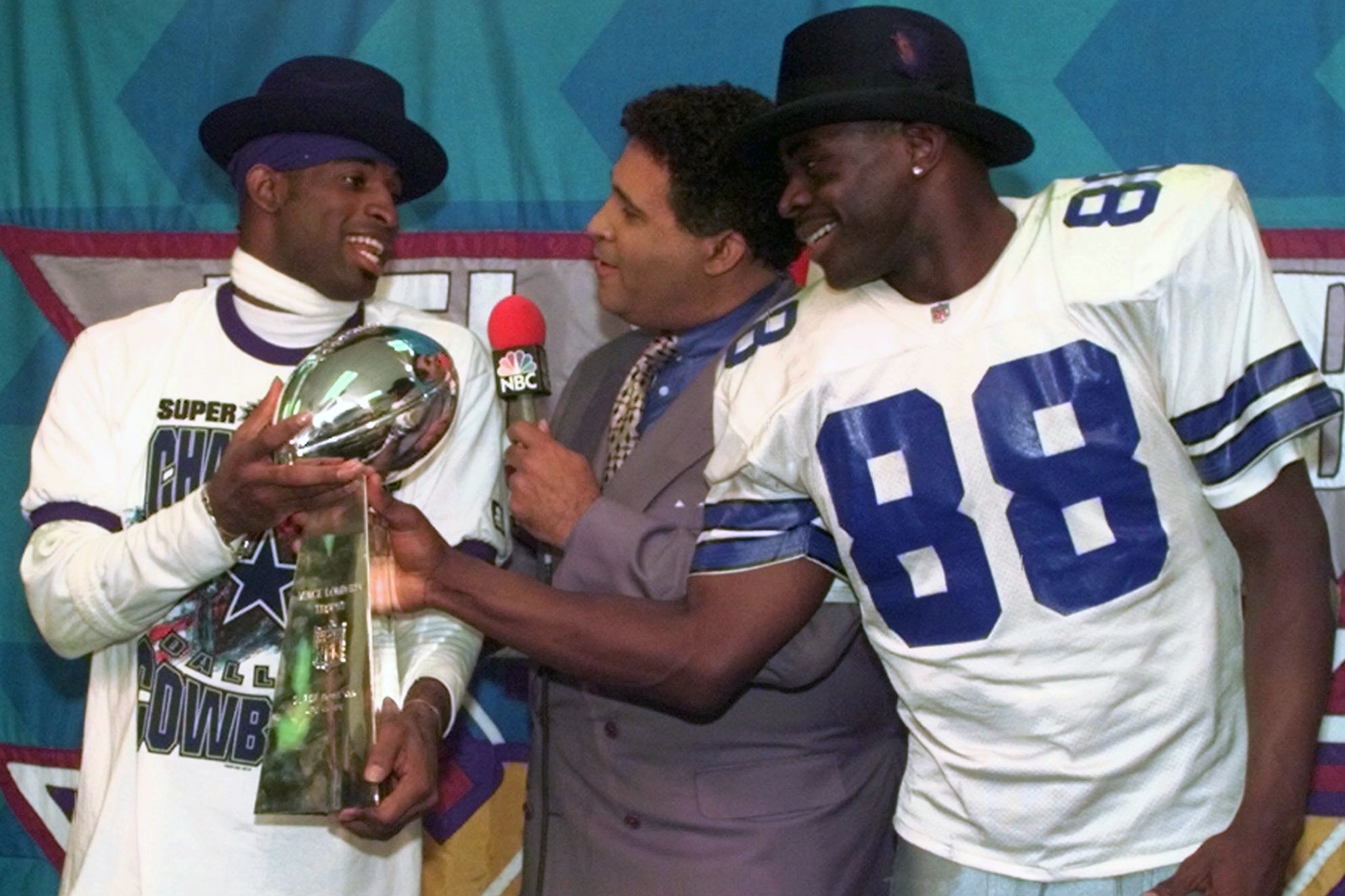 Dallas Cowboys cornerback Deion Sanders (left) and running back Michael Irvin (88) share the Vince Lombardi trophy as NBC commentator Greg Gumbel interviews the two after Super Bowl XXX in Tempe, Ariz., on Jan. 28, 1996.