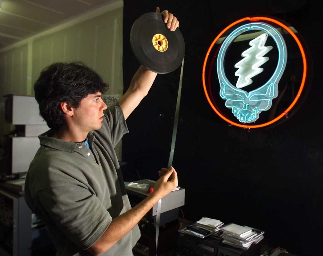 In this August 7, 2000, photo, David Lemieux holds up a piece of 16 mm motion picture film that has been unfurled from a reel. A neon sign featuring the Grateful Dead's emblem of a skull with a lightning bolt across the top hangs on a wall nearby.