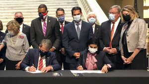 Georgia Gov. Brian Kemp, left, and Centers for Medicare and Medicaid Services Administrator Seema Verma, right, sign waivers allowing Georgia to institute work requirements for certain Medicaid recipients at the state Capitol in Atlanta, Oct. 15, 2020.