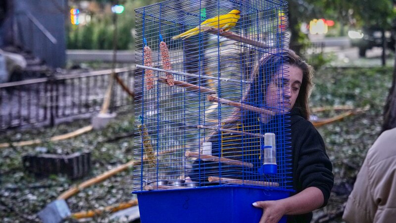 A woman carries a cage with a parrot as she leaves her damaged house following a Russia missile attack in Kyiv, Ukraine, Sunday, July 19, 2026. 