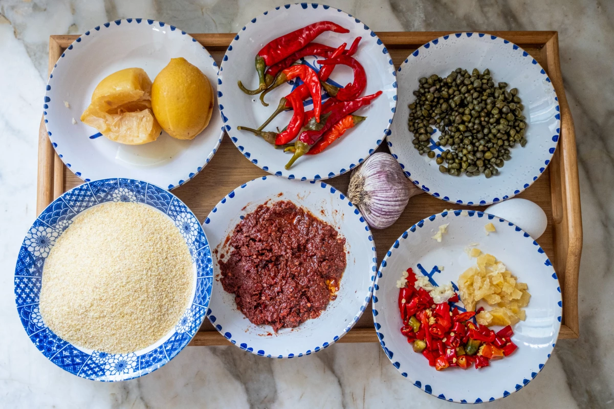 Ingredients for hsou are laid out on a platter. Top row, left to right: pickled lemons, pickled red peppers and capers; bottom row, left to right: semolina, harissa, diced pickled lemons and pickled peppers.Â