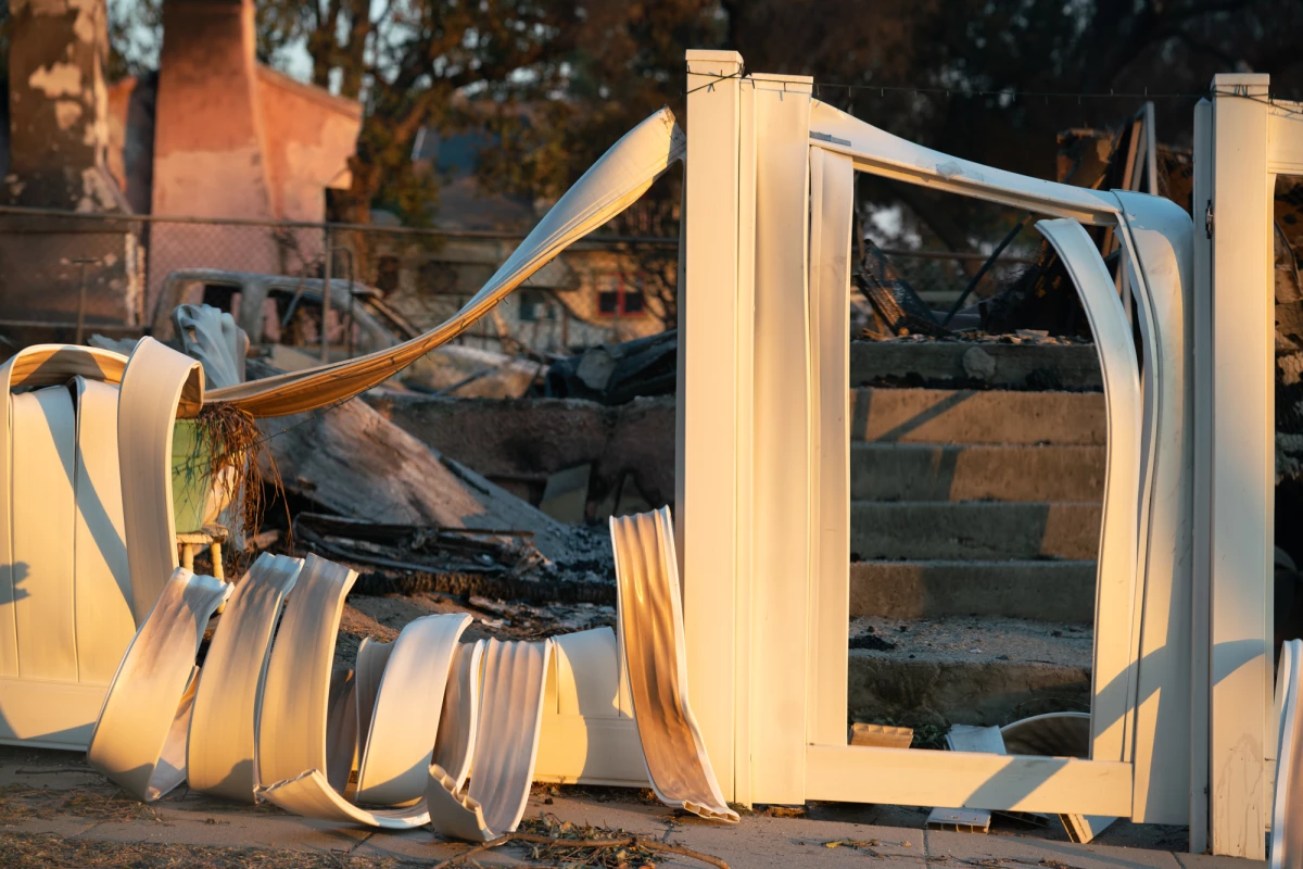 A part of a melted fence spills over a yard in Altadena, Calif., after the Eaton Fire devastated the neighborhood in 2025. Recovering from such a major disaster often takes years and relies on federal funding.