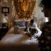 Thomas Guzowski greets his dogs — a 13-year-old shih tzu and a 15-year-old terrier poodle mix — as they climb onto the bed on July 18 in Redlands, California. The bed has a white bedspread and two blue pillows. String lights hang on the wall behind the bed.