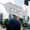 A protestor holds a sign that says "Protect the CDC;" it is shaped like a vaccine syringe.