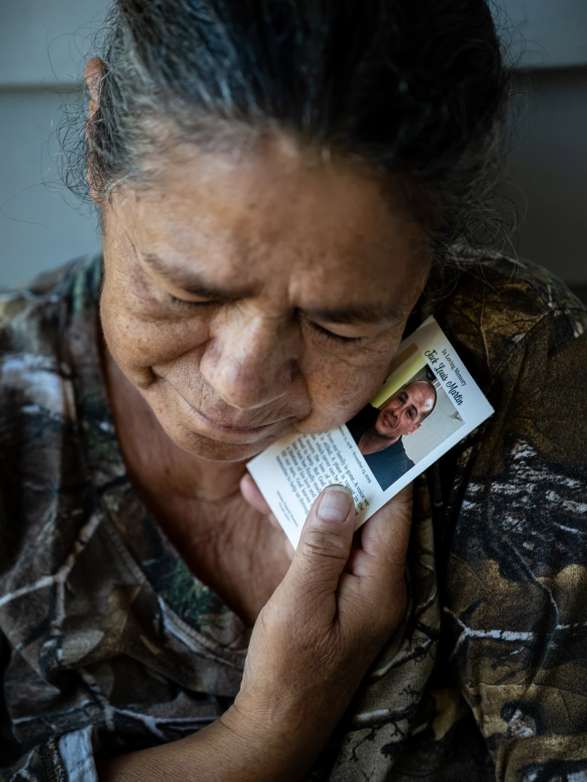 Maria del Carmen Martin, 69, holds a memorial card from the funeral of her late son, Jack Martin, a journeyman plumber who died in a workplace accident in 2019 when a trench that he was laying pipe in collapsed.