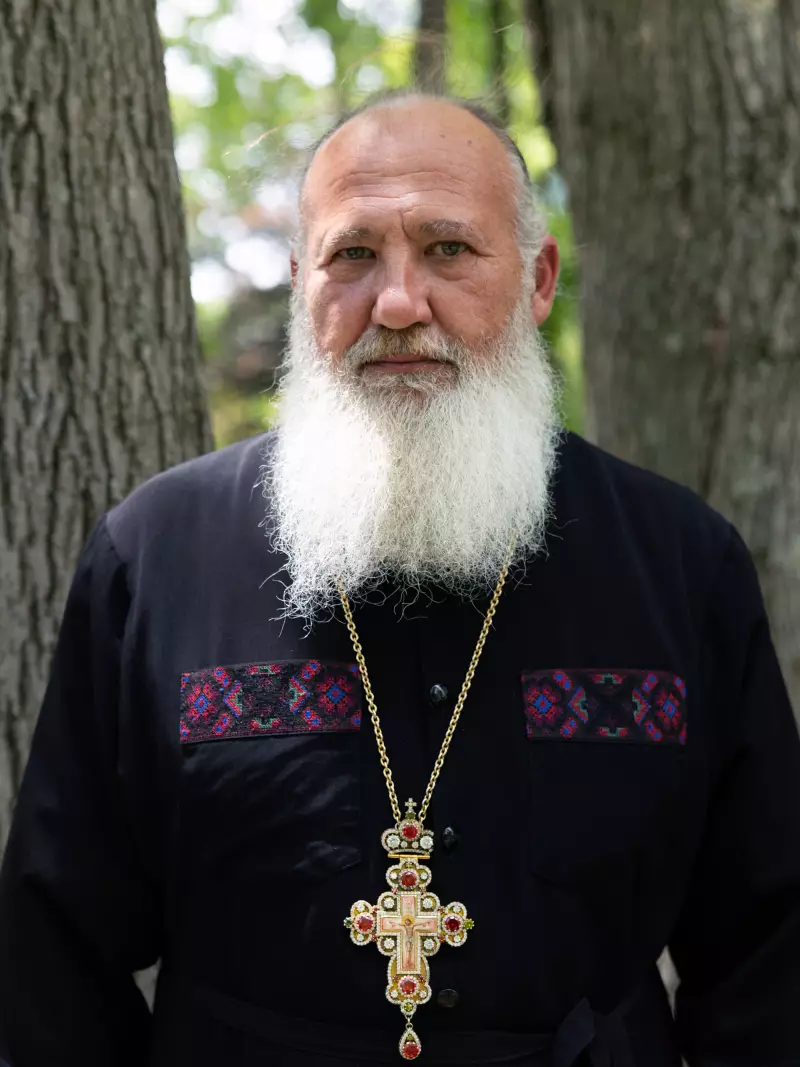 Father Taras Naumenko poses for a photo on June 21, 2026. He is wearing a cross around his neck and is photographed from about the waist up. He's standing outdoors, and two tree trunks rise behind him.