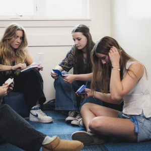 Two teen girls and two young women sit in a circle on a blue carpet. 