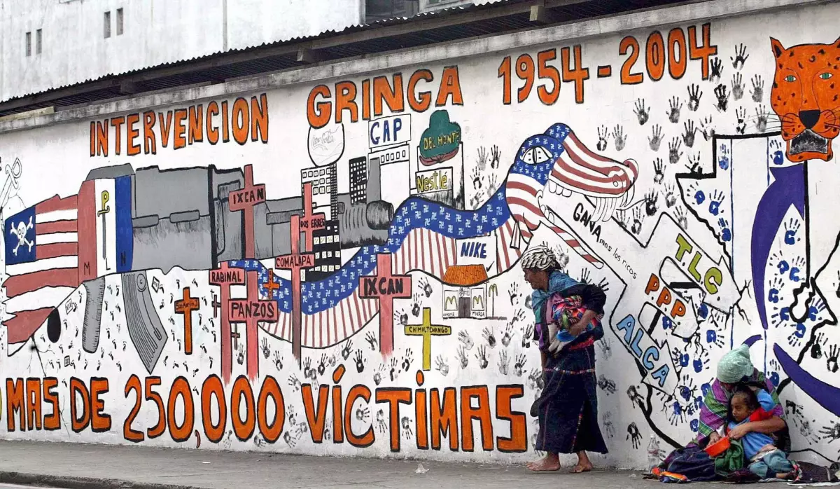 Indigenous women beg in Guatemala in June 2004 in front of a propaganda mural that speaks against U.S. interventions in the region.