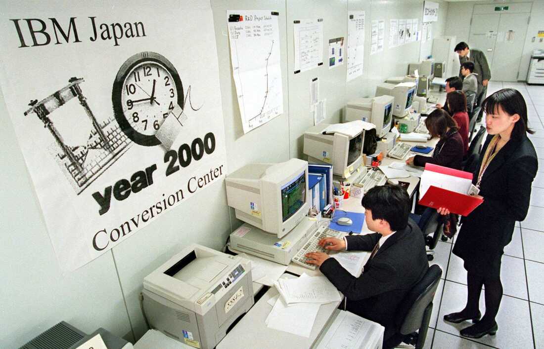 Los ingenieros de IBM Japón se sientan frente a una fila de computadoras en una sala de conferencias, trabajando para convertir el software de sus clientes, incluidos bancos y gobiernos locales, para protegerlos contra los efectos potencialmente destructivos. "error del milenio" problema informático.