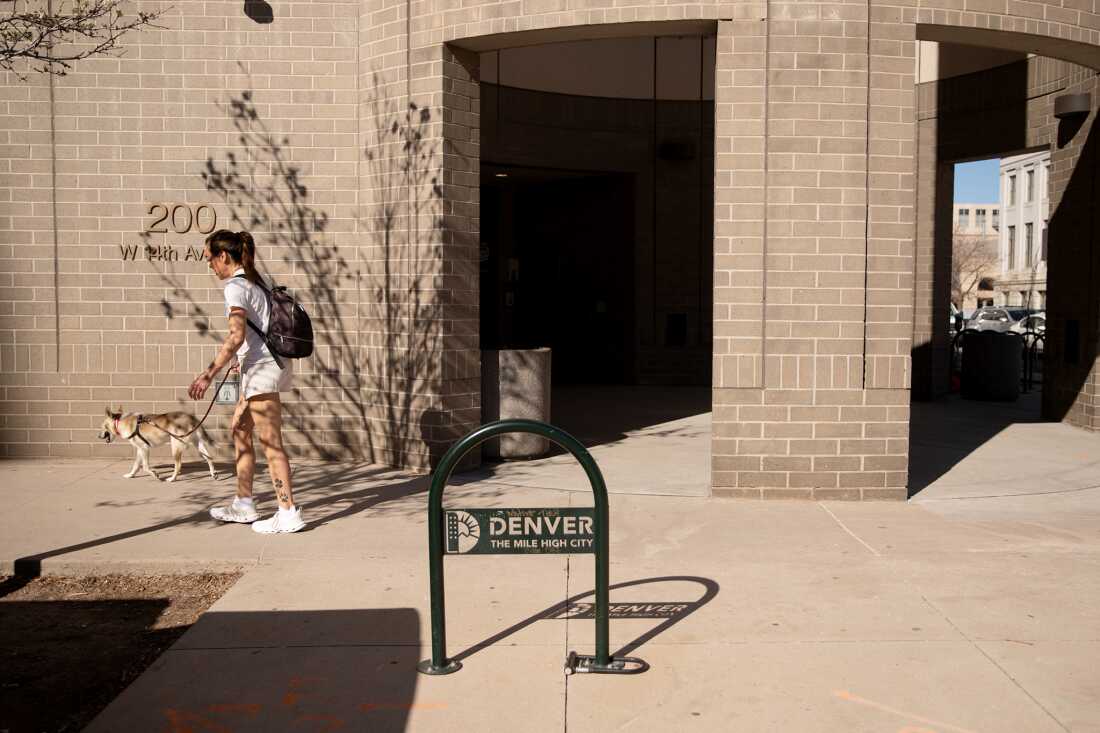 A woman walks her dog past the Denver Elections building, which is made of brown bricks.