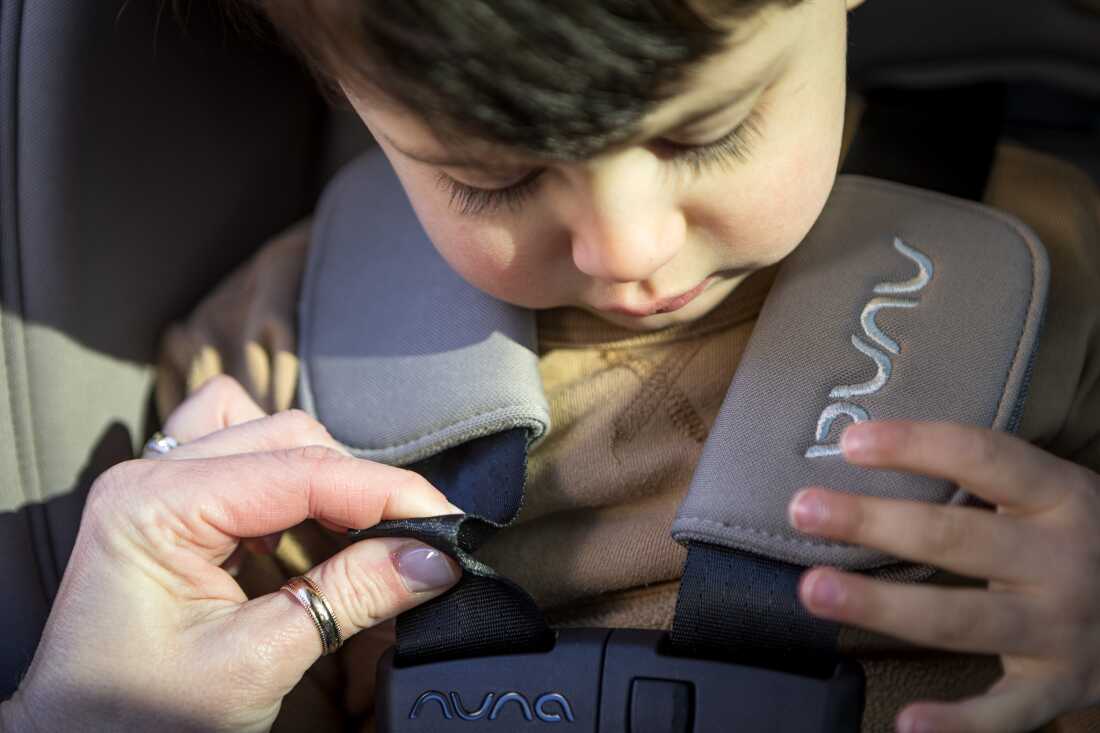 神奈川捏着汽车座椅上的安全带,而一个小男孩坐在座位上。她说,能够捏住织带意味着安全带太松了。