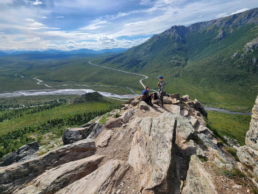 Hikers rest on an outcropping on the Savage Alpine Trail in Denali National Park on July 26, 2026. The sole road through the park is seen below. Travel restrictions on the 92-mile park road begin at the 15-mile mark, at the Savage River, seen in the background.