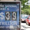 "THE NATIONAL DEBT IS $39 TRILLION AND GROWING." Cars pass by on a road on the right side of the frame.