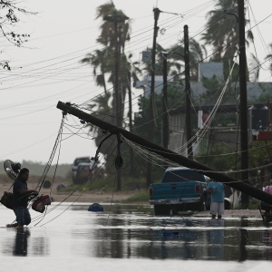 A man carries items through floodwater past downed electric lines after the passing of Hurricane Polo in Puerto San Carlos, Baja California Sur state, Mexico, Tuesday, Sept. 29, 2026.