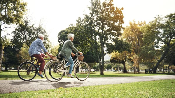 A man and a woman, both with gray hair, riding bikes on a paved path on a sunny day.