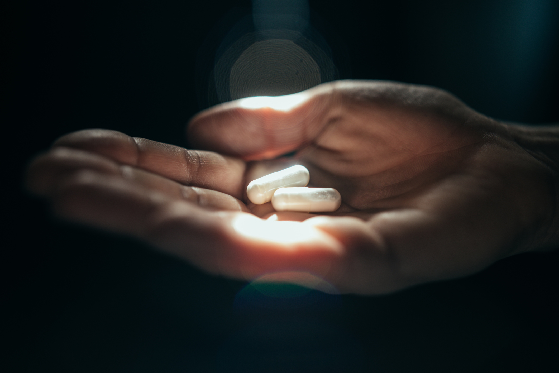 Hand holding 2 pills in sunlight.