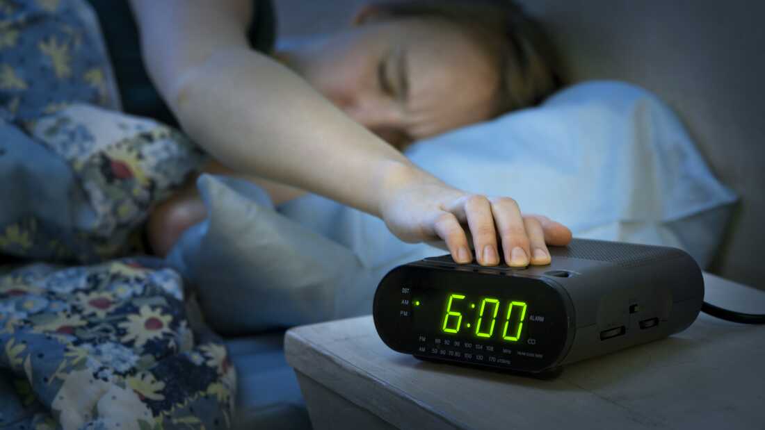Young woman pressing snooze button on early morning digital alarm clock radio