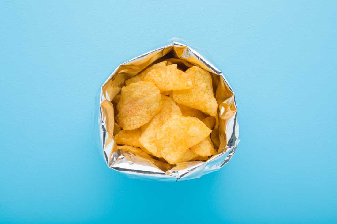 This photo shows a bag of potato chips in an open foil bag, photographed from above. The bag is standing on a light blue surface.