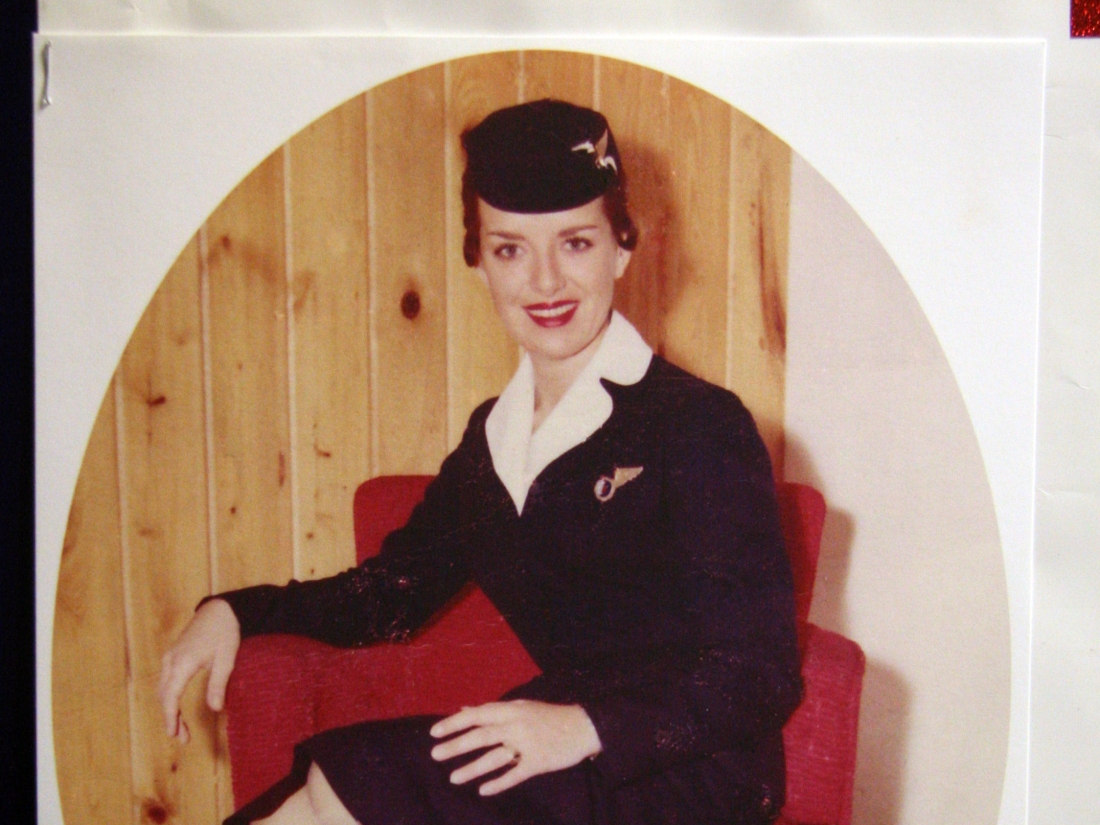 A young female flight attendant in uniform poses in a red chair.
