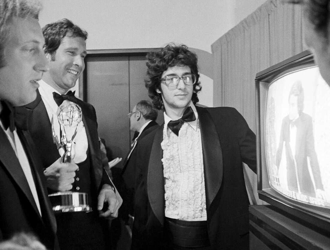 Chevy Chase, center, holds his Emmy Award as he watches producer Lorne Michaels accepting another Emmy for SNL, while writers Alan Zweibel, left, and Tom Davis look on in 1976.