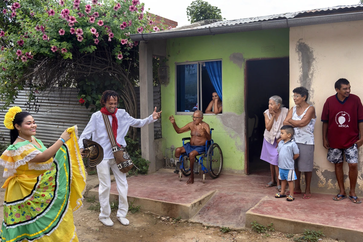 Melgen Melendez Baena, a cumbia dancer from Barranquilla, holds up his hand as Cristobal Perez Santos, 72, watches the parade of gaitero groups and dancers from his wheel chair as they move through the town and then to the cemetery to pay tribute to the late gaiteros on Aug. 14, 2022, in San Jacinto, Bolivar, Colombia.