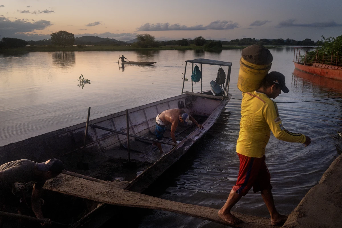 Workers unload sand at the El Cesar dock in El Banco, Colombia, on Aug. 8, 2022. In the distance, a fishing boat is also seen returning to the dock.