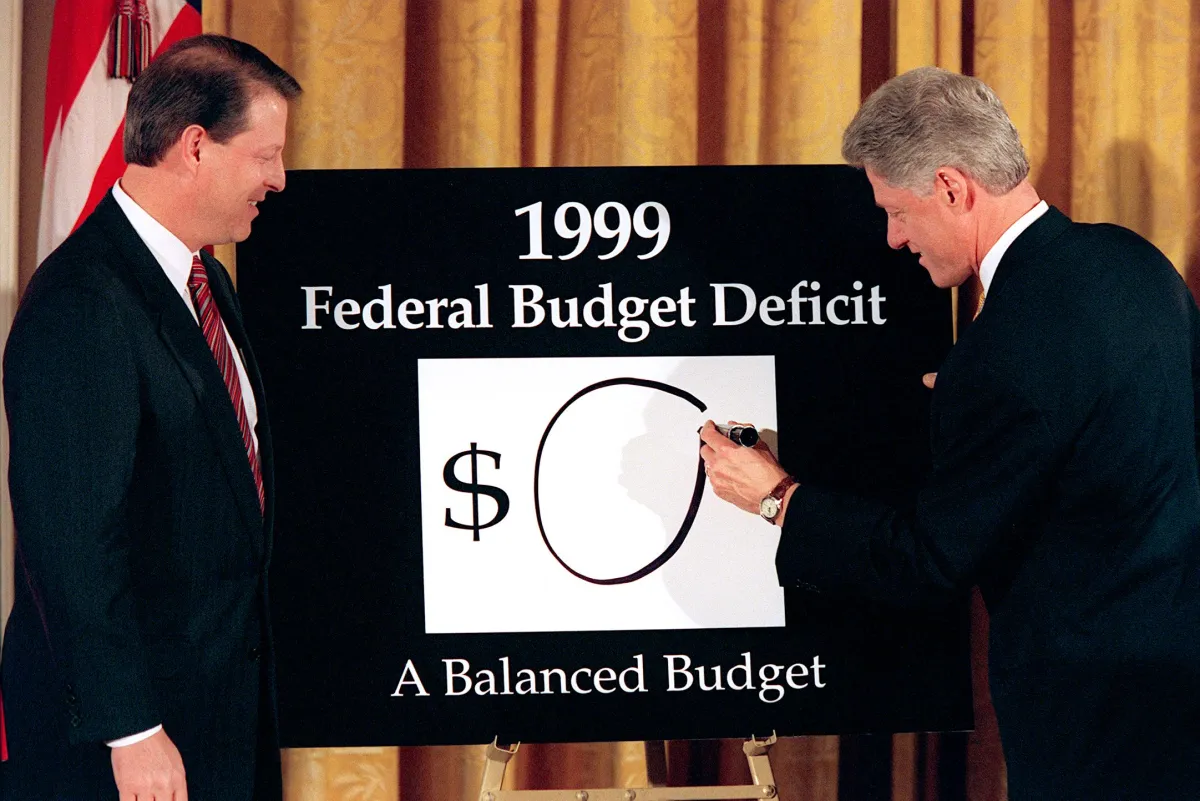 Vice President Al Gore (left) looks on as President Bill Clinton (right) places an '0' on the board showing what the federal deficit will be after unveiling his balanced budget plan for 1999.