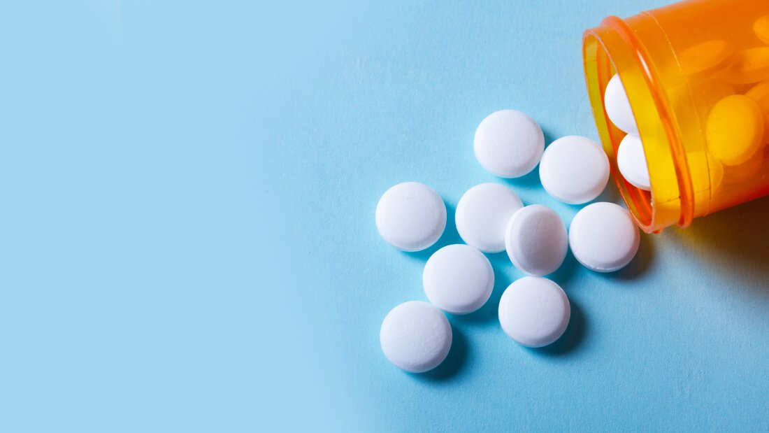 قرصهای سفید گرد در بطری نارنجی، نمای نزدیک در بنر پسزمینهٔ آبی با فضای خالی