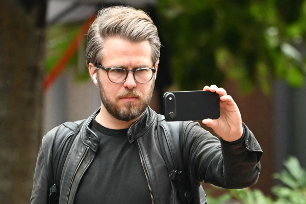 Miles Taylor, former chief of staff at the Department of Homeland Security during President Donald Trump's first term, holds up his phone outside of the Albert V. Bryan United States Courthouse ahead of the arraignment hearing for former FBI director James Comey in Alexandria, Virginia on October 8, 2025.