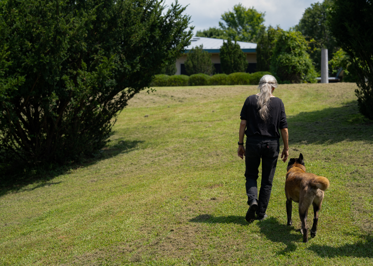 Sally Mann on the grounds of her Virginia home, accompanied by one of her rescued Belgian Malinois dogs.