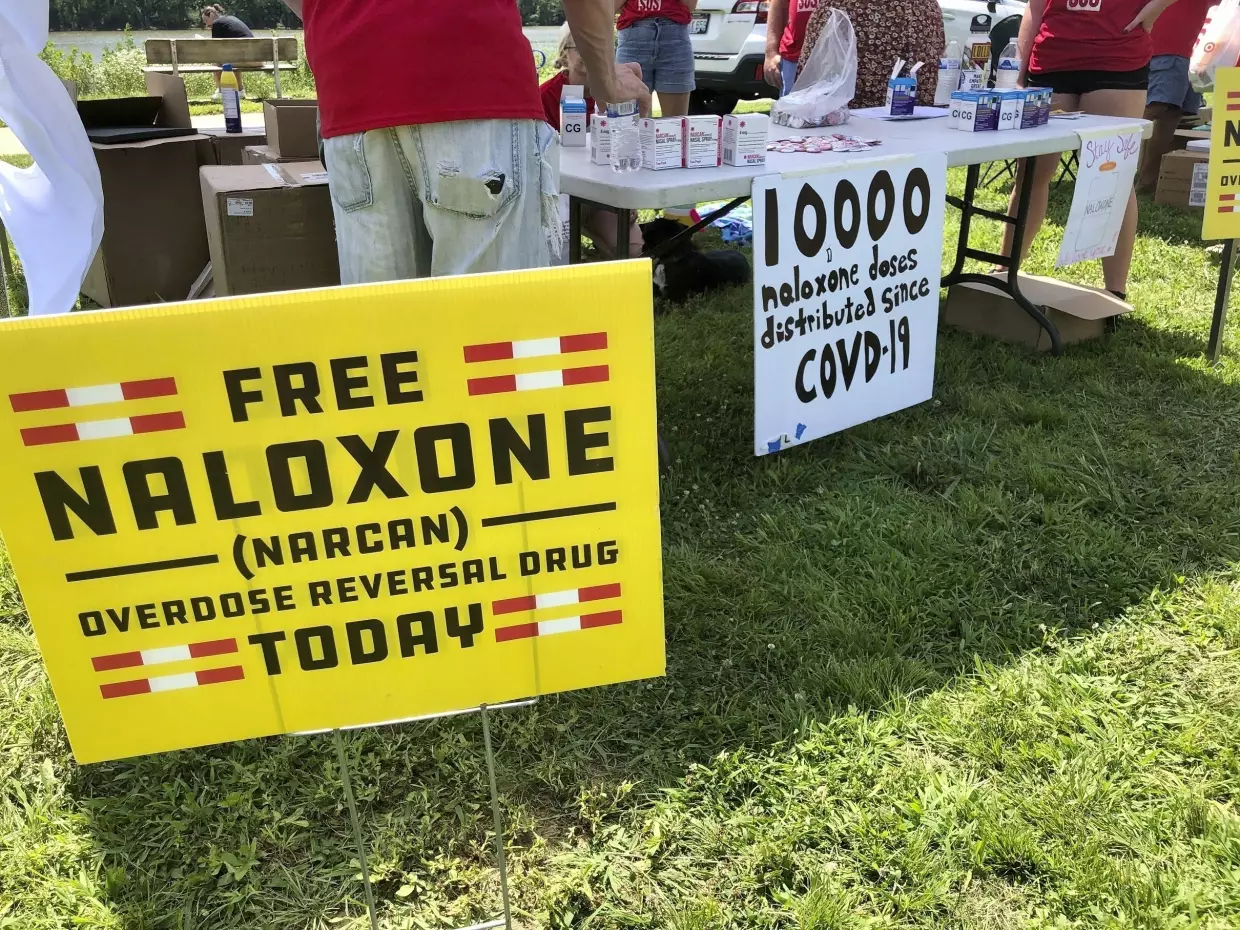 In this file photo, signs are displayed at a tent during a health event in Charleston, W.Va.  Public health officials say the spread of naloxone, also known as Narcan, has dramatically reduced overdose deaths in the U.S.