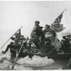This black-and-white image shows George Washington crossing the Delaware River during the American Revolutionary War in 1776. He's standing in a rowboat as men around him paddle the boat through the river, which has large chunks of ice floating in it. Two men behind him in the boat hold a partially unfurled American flag.
