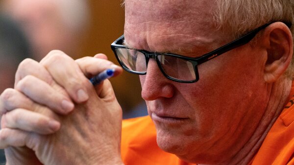 Alex Murdaugh wearing black-framed glasses with his hands clasped while holding a pen in front of his face. 