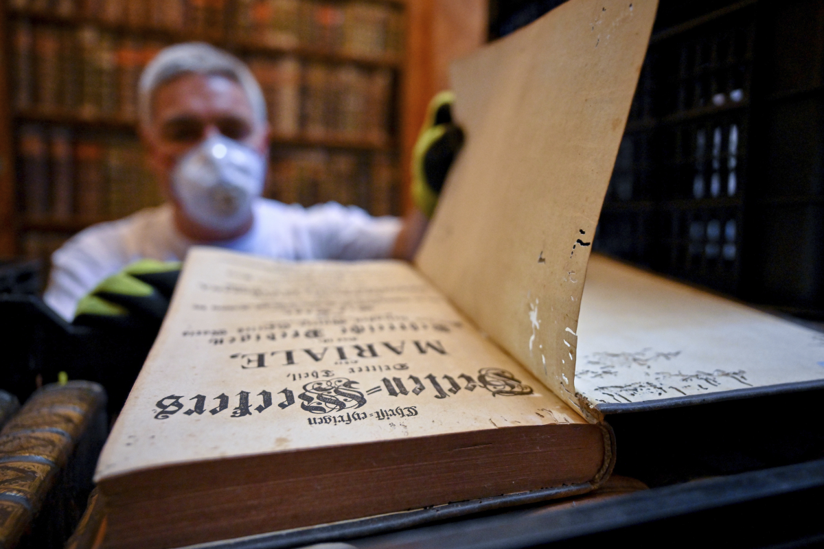 In this photo provided by Pannonhalma Archabbey, a restorer shows an old book with holes in its pages due to a drugstore beetle infestation, at the Pannonhalma Archabbey's library in Pannonhalma, Hungary on July 3.