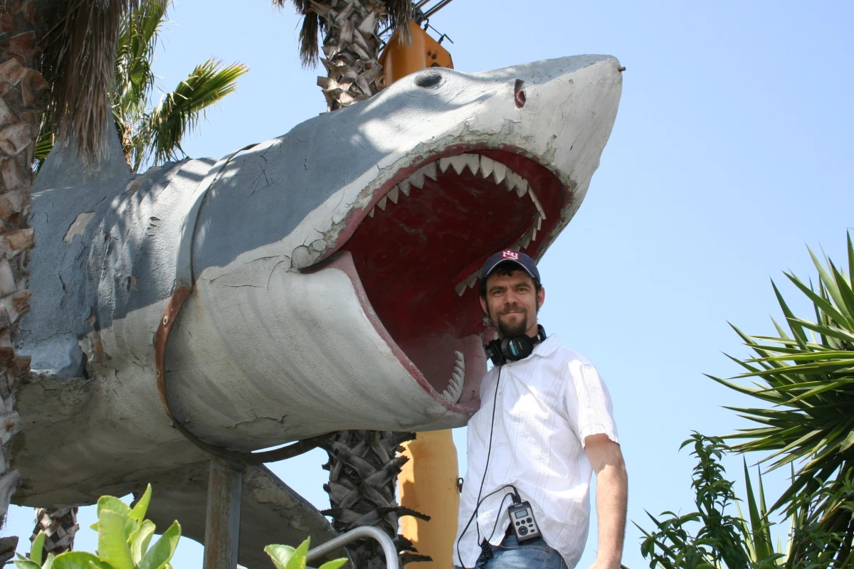 NPR's Cory Turner at the junkyard in 2010, with Junkyard Bruce, the last shark made from the original Jaws mold. It was later restored to its former glory and hung in a place of honor at the Academy Museum..