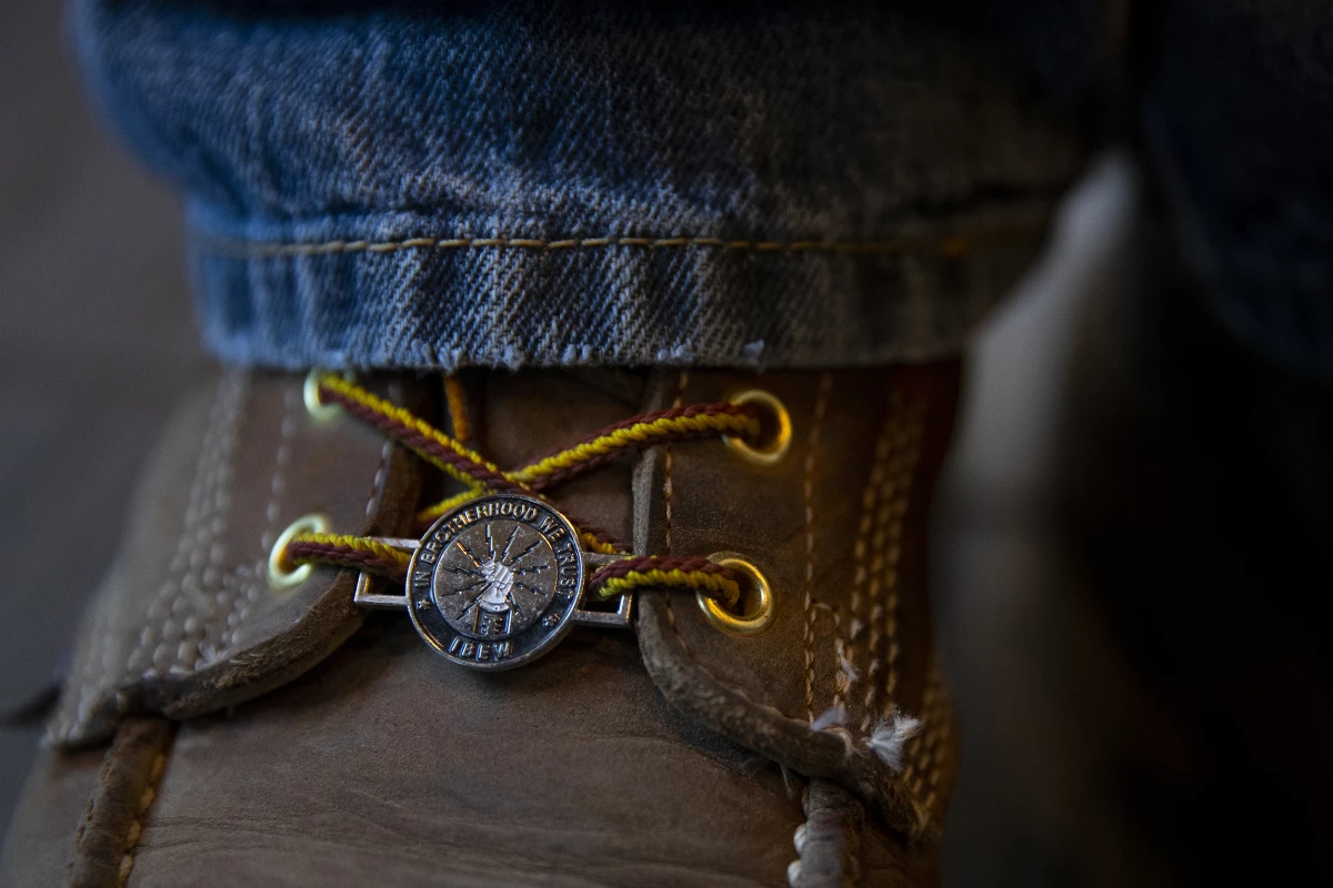 Electrician Jimmy Ortega wears an IBEW boot charm that reads, 'in brotherhood we trust,' at IBEW Brotherhood Night on Thursday, July 17, 2025, at Monkey N'Around Pizza in Quincy, Washington.