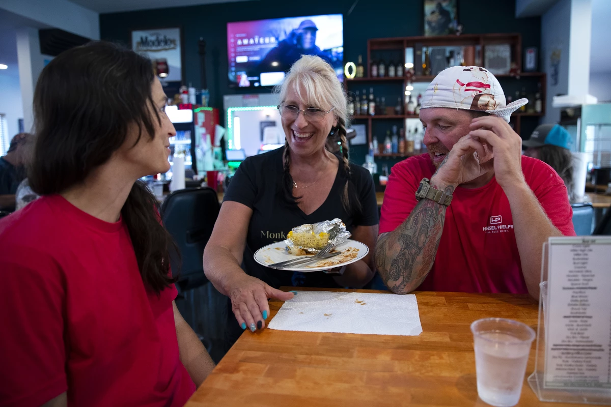 Sharyl Smith, center, owner of Monkey N'Around Pizza, laughs with electricians Micki Bohman, left, and Mark Gruszkiewicz, right, during IBEW Brotherhood Night on Thursday, July 17, 2025, in Quincy, Washington. Bohman and Gruszkiewicz met at a data center job site and got married a year and a half ago.