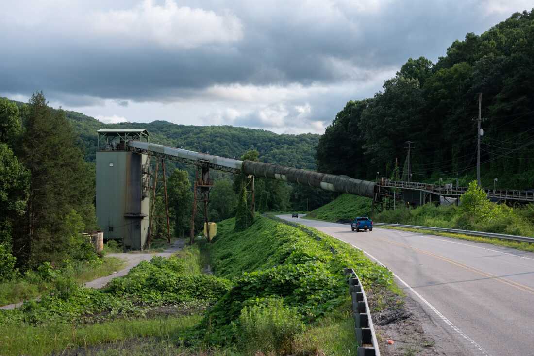 The long metal chute of a coal preparation plant crosses over U.S. 23 in Appalachia, Virginia. Tree-covered mountains rise in the background.