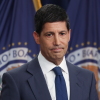 This photo shows Federal Reserve Chairman Kevin Warsh. He's wearing a blue suit, white shirt and blue tie. Behind him are two flags with the seal of the Federal Reserve on them.