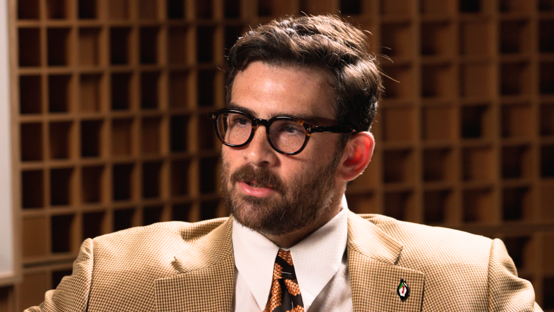Hasan Piker is seen from the shoulders up wearing a light brown suit jacket.